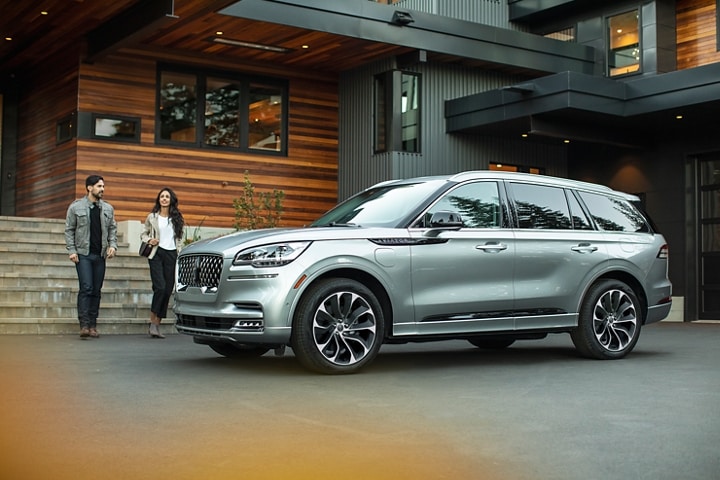 Couple approaching a 2023 Lincoln Aviator® Grand Touring model parked in the driveway of a modern home