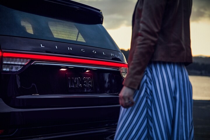Person stands behind a 2023 Lincoln Aviator® as the Lincoln® Embrace illuminates the taillamps