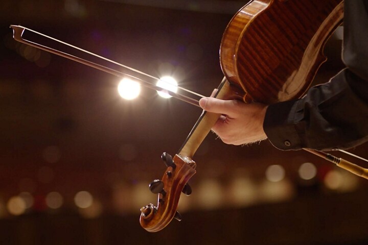 Hand holding a violin in a concert hall