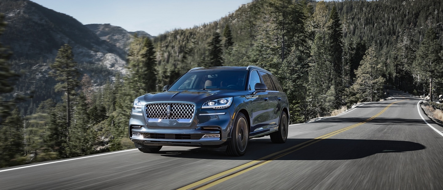 A 2024 Lincoln Aviator is being driven on a tree-lined mountain road