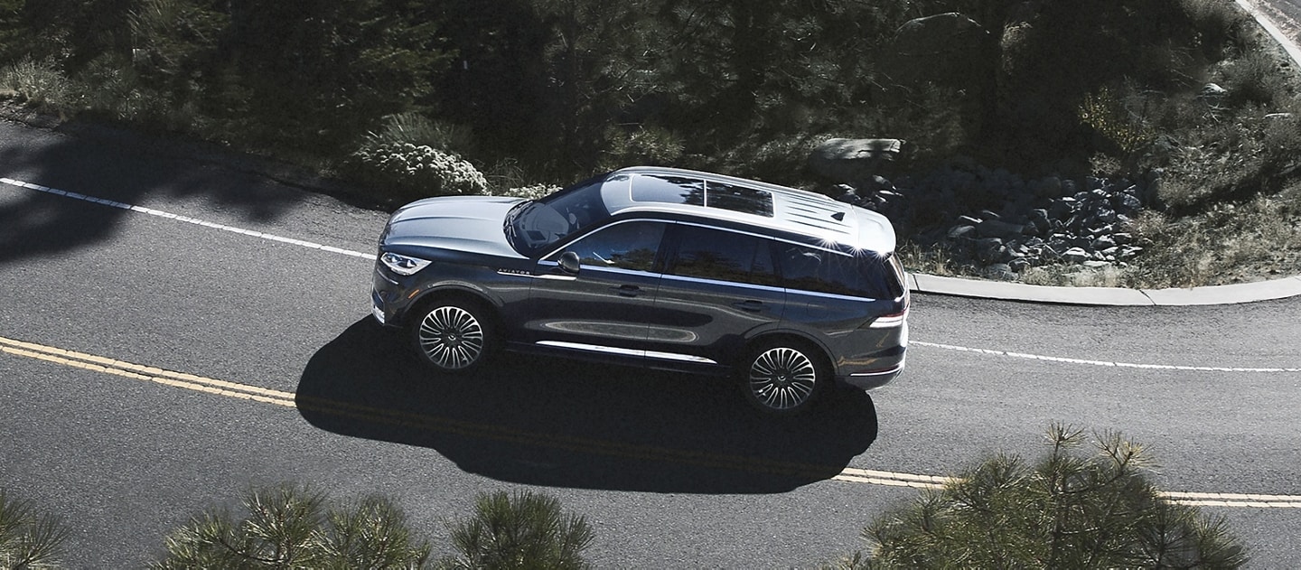 A 2024 Lincoln Aviator driving down a winding, tree-lined road
