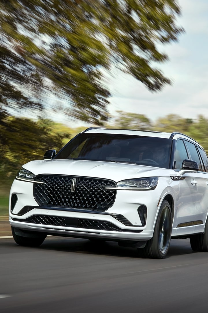 A 2025 Lincoln Aviator is shown driving on a highway near a forest