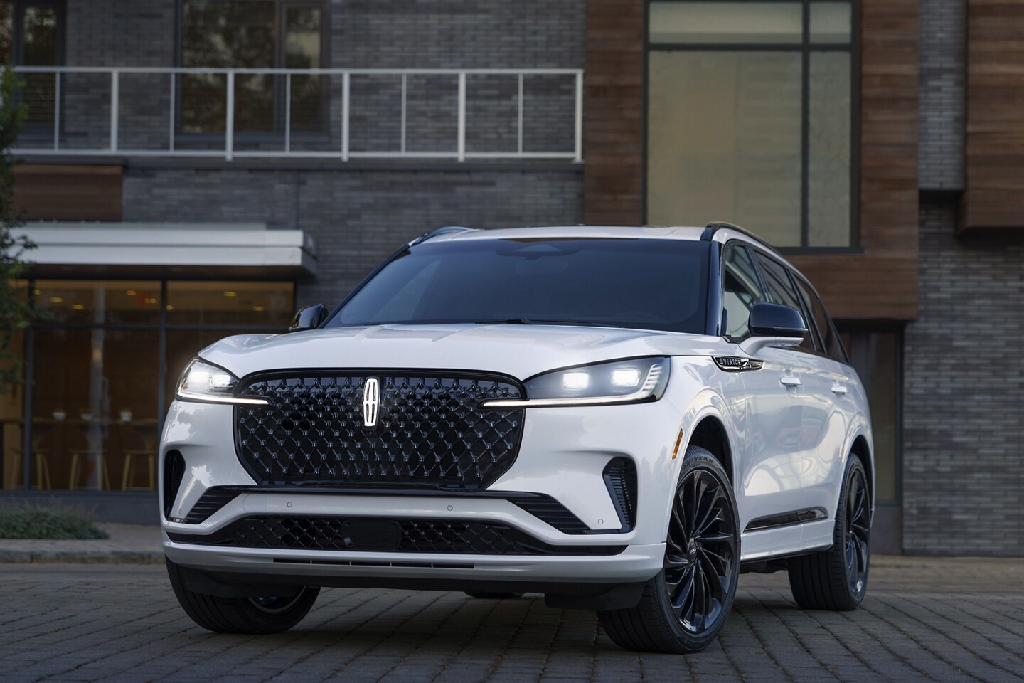 A 2025 Lincoln Aviator Reserve is parked in front of a restaurant with its headlamps on