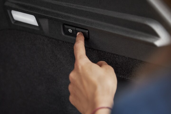 A woman pushes the easy fold power button in the cargo space to effortlessly fold seats and open up cargo space