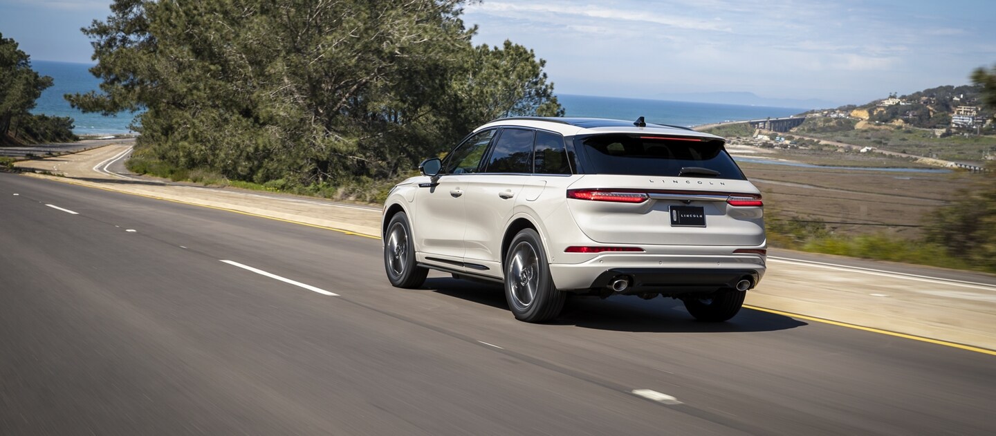 A 2023 Lincoln Corsair Grand Touring model is being driven next to a scenic expanse ocean fading into the horizon