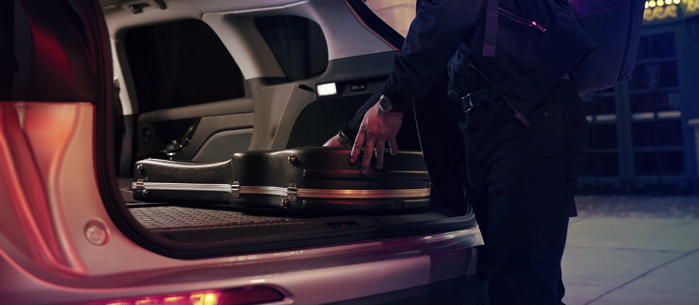 A musician slides his guitar case into the cargo area of a 2023 Lincoln Corsair SUV with the rear seats folded flat