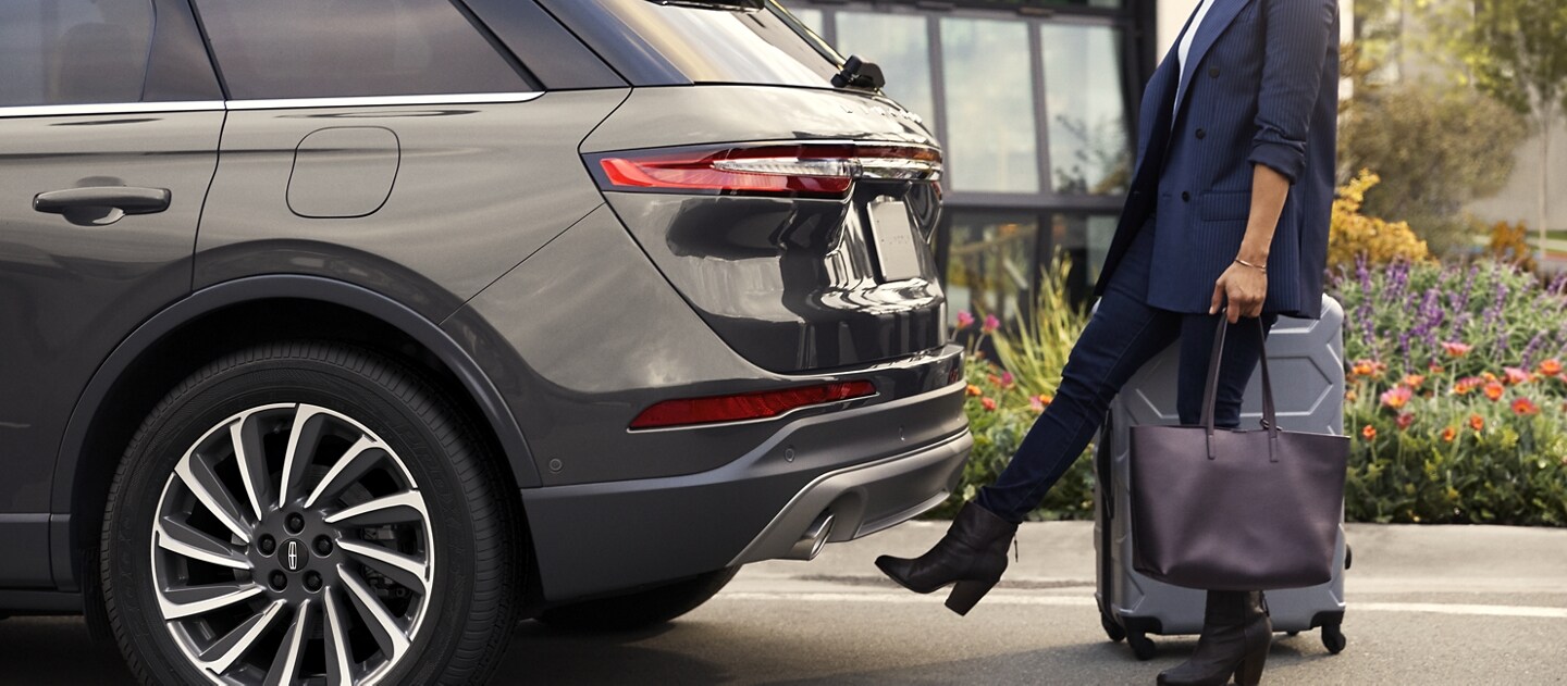 A woman with luggage and a bag opens the hands free power liftgate by kicking her foot under the bumper