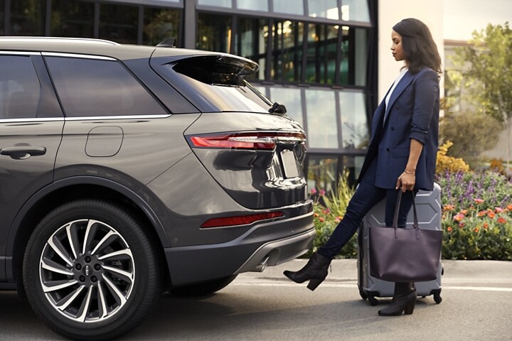 A woman with luggage and a bag easily opens the hands free power liftgate by kicking her foot under the bumper