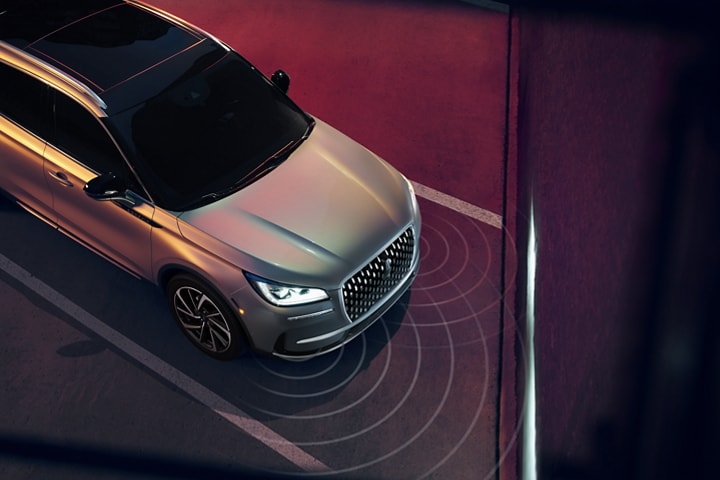 A 2023 Lincoln Corsair SUV is being guided into a diagonal parking space as the headlamps illuminate the wall ahead