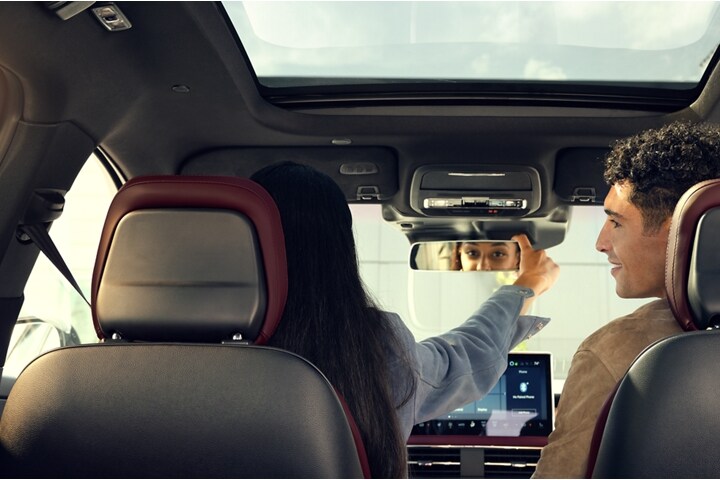 A blurred face is shown in the reflection of the sleek frameless rearview mirror as soft lights glow through the windshield