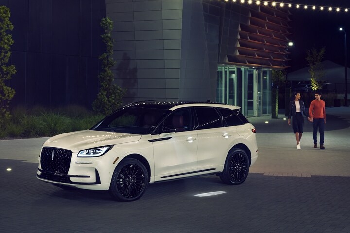 A couple approaches a 2023 Lincoln Corsair SUV at night greeted by the soft glow of the Lincoln Embrace