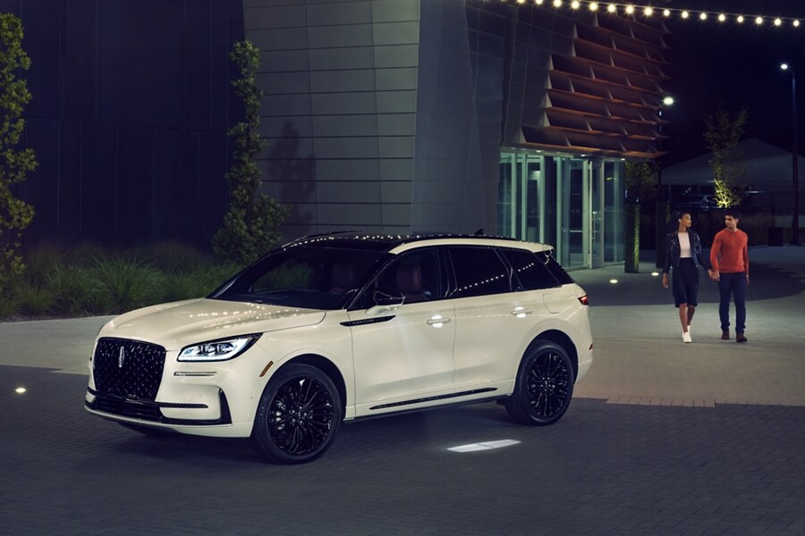 A driver approaches a 2023 Lincoln Corsair SUV at night greeted by the soft glow of the Lincoln Embrace