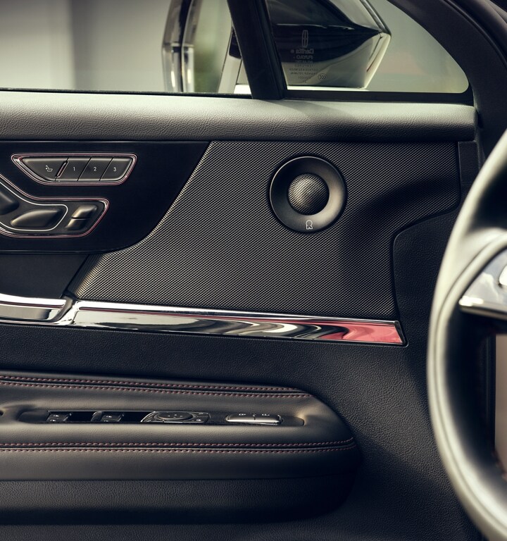 The muted black texture of a Revel door speaker is elegantly integrated into design among contrasting chrome controls