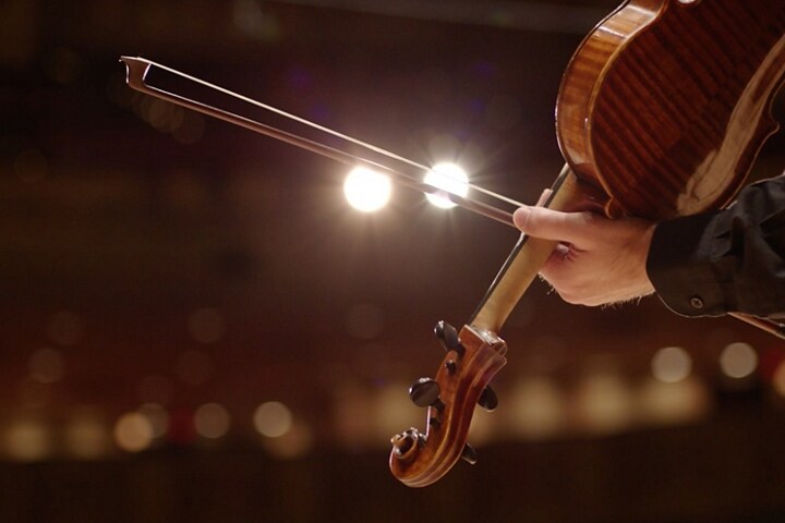 A person draws a bow across the string of a violin alluding to the chimes in a 2025 Lincoln Corsair