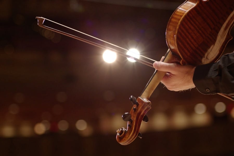 A person draws a bow across the string of a violin alluding to the chimes in a 2025 Lincoln Corsair