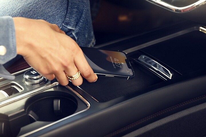A hand places a mobile phone on the available wireless charger inside a 2026 Lincoln Corsair