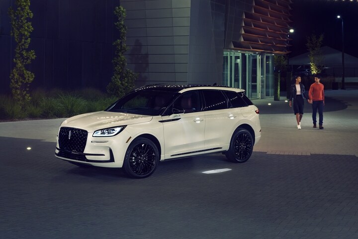 A couple approaches a 2026 Lincoln Corsair SUV as the Lincoln Embrace illumination guides the way