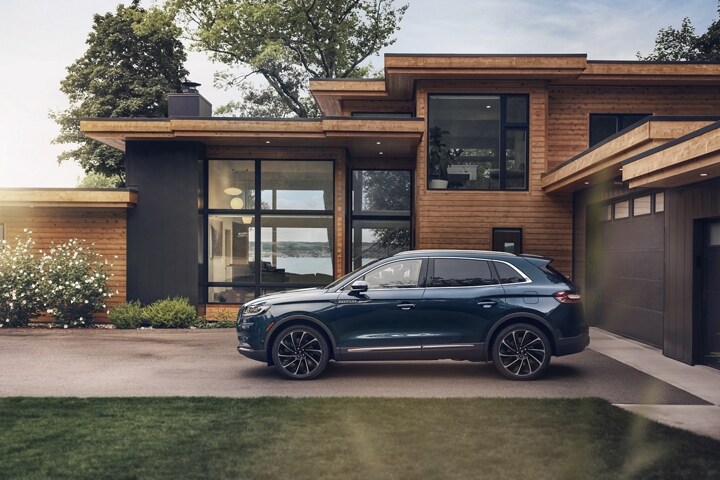 A 2023 Lincoln Nautilus SUV is parked outside a modern lakehouse