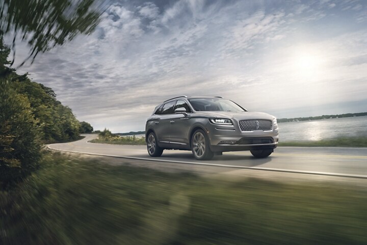 A 2023 Lincoln Nautilus SUV in Silver Radiance is being driven down a lake side road