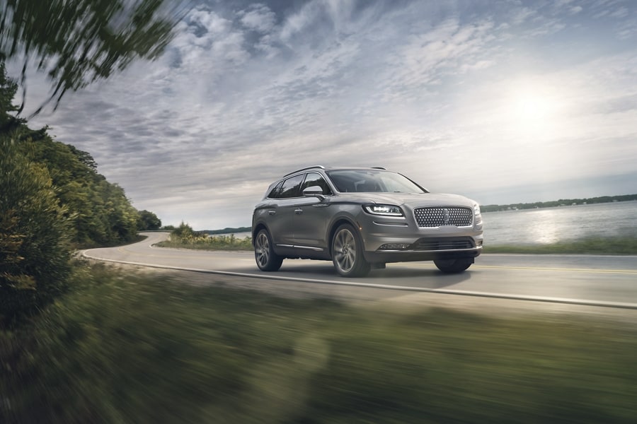 A 2023 Lincoln Nautilus in Silver Radiance is being driven down a lakeside road