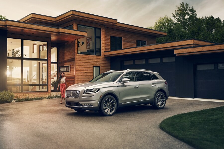 A person approaches a 2023 Lincoln Nautilus SUV in Silver Radiance parked outside a mid-century modern home