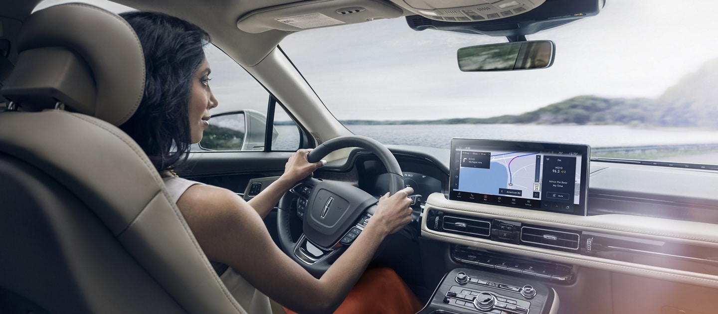 A woman is driving a 2023 Lincoln Nautilus SUV as the navigation application on the center touchscreen guides her course