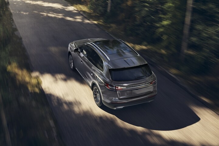 A 2023 Lincoln Nautilus SUV is shown being driven along a forest lined road