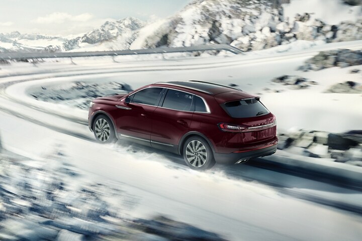 A 2023 Lincoln Nautilus SUV is shown being driven on a snow covered road with a sharp turn ahead