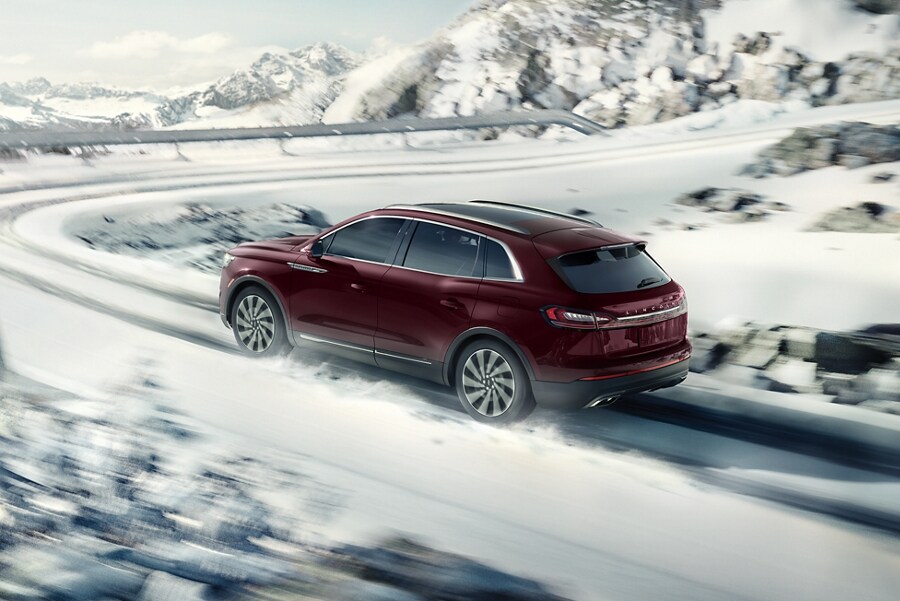 A 2023 Lincoln Nautilus SUV is shown being driven on a snow-covered road with a sharp turn ahead