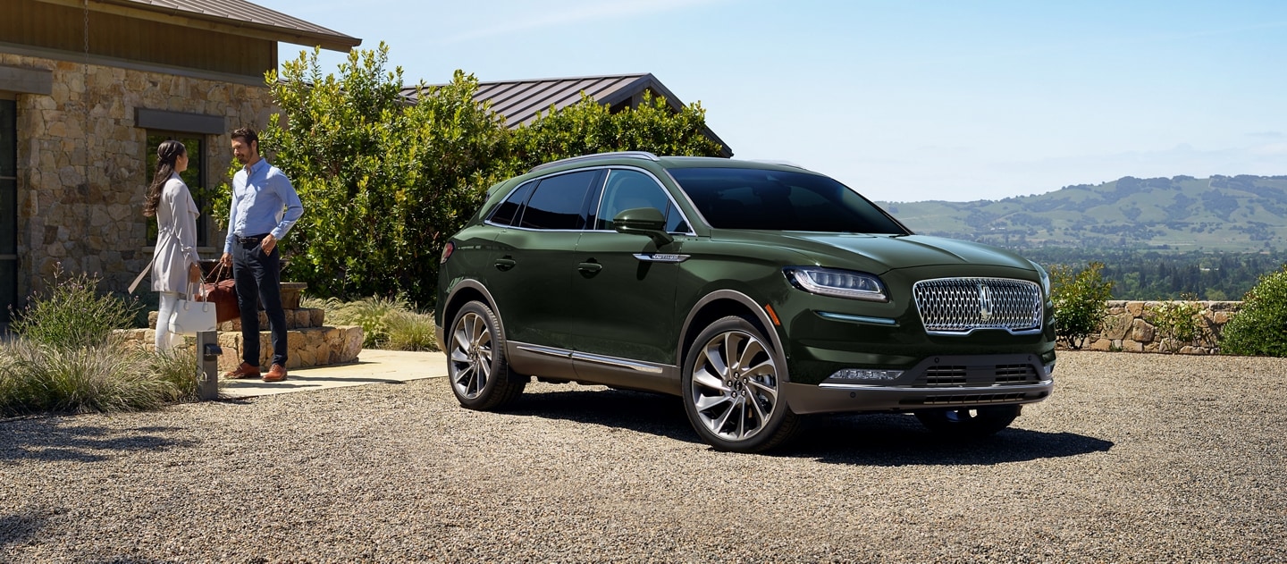 A couple is standing outside a cobblestone home next to a 2023 Lincoln Nautilus SUV