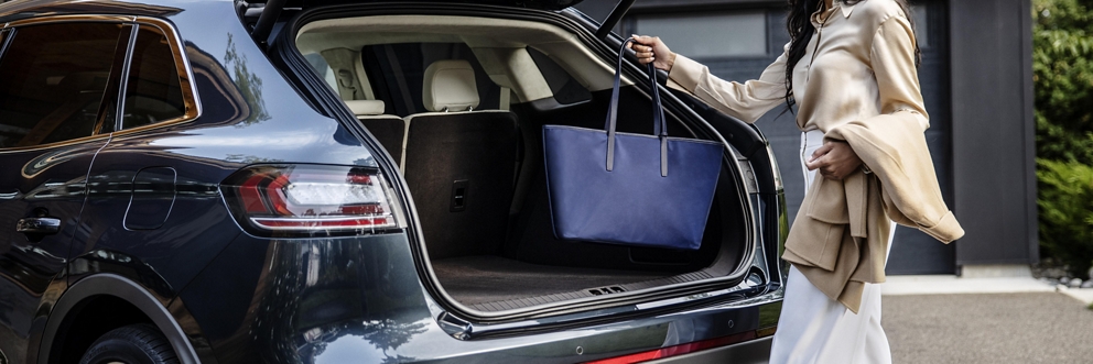 A woman placing a purse into the trunk of a lincoln vehicle.