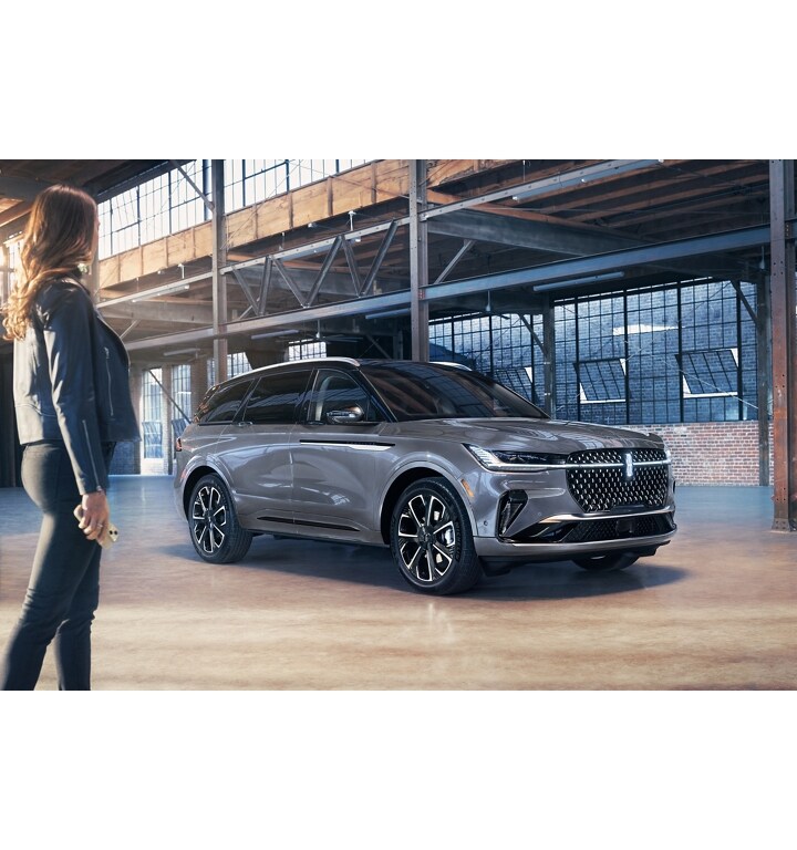 A smartphone is being held in a woman’s hand as she walks toward a 2025 Lincoln Black Label Nautilus SUV