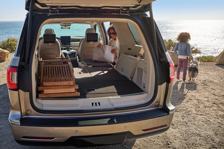 The second and third rows of a 2021 Lincoln Navigator are folded flat as a woman unloads a beach bag with a little girl and her dog