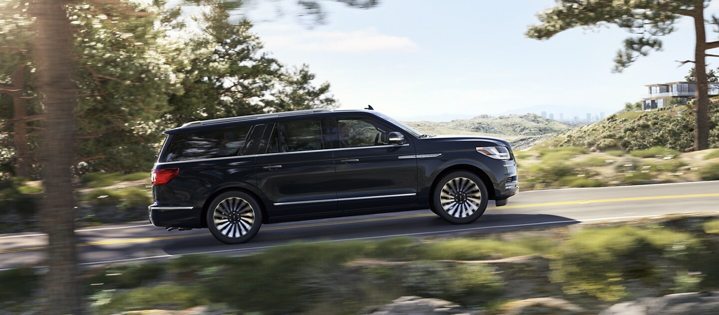 A 2021 Lincoln Navigator in Infinite Black is being guided up an incline surrounded by greenery with a loft and cityscape fading away in the back