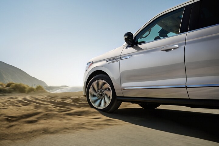 A 2023 Lincoln Navigator SUV with available four-wheel drive is being driven in sandy terrain