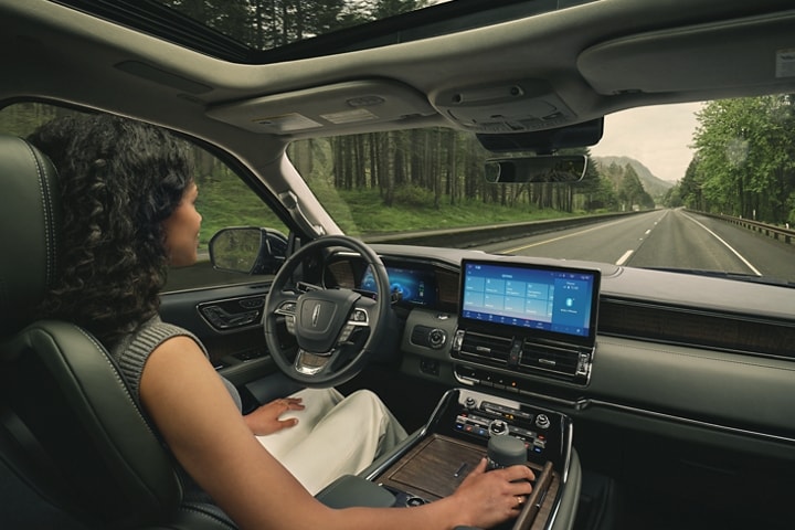 A woman in the driver seat of a 2023 Lincoln Navigator SUV relaxes with hands free driving technology engaged