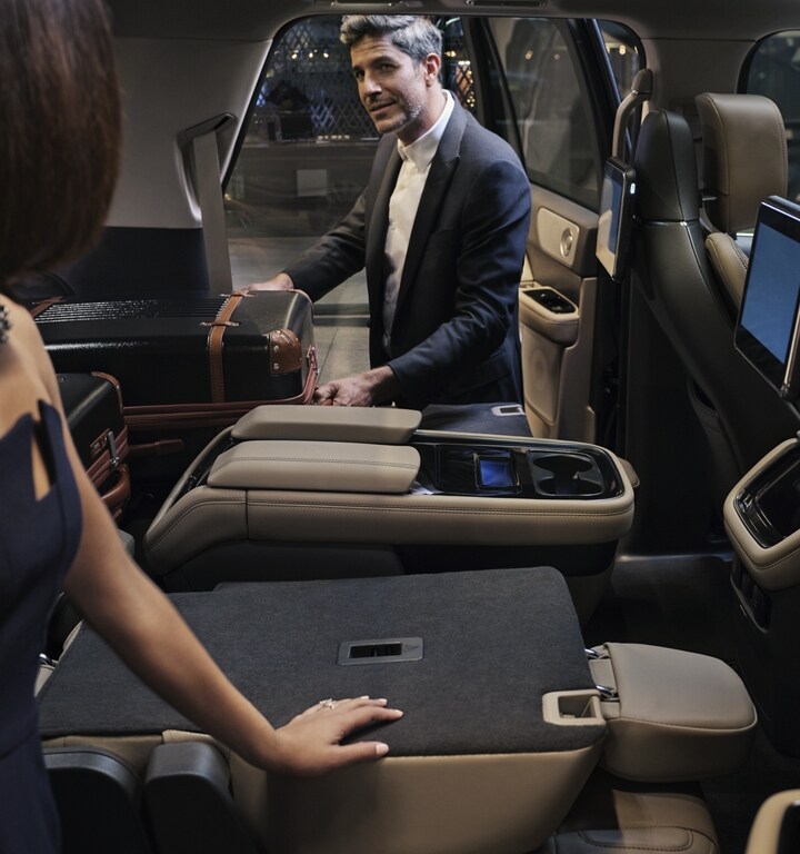 A man is pulling a suitcase out of the folded-flat second-row seat of a 2023 Lincoln Navigator® SUV