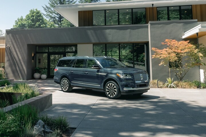 A 2023 Lincoln Navigator® SUV is parked in front of a beautiful mid-century modern home on a sunny day