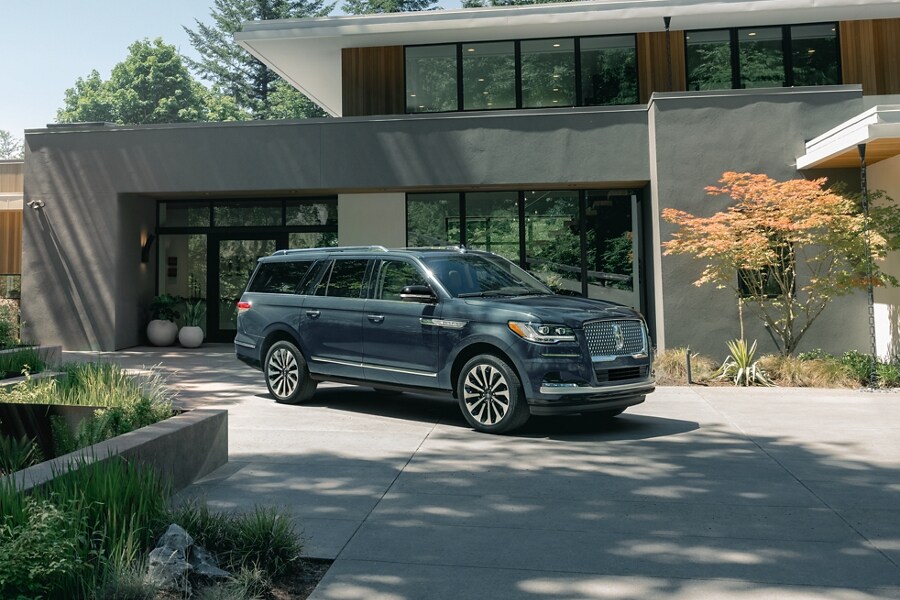A 2023 Lincoln Navigator® SUV is parked in front of a beautiful mid-century modern home on a sunny day