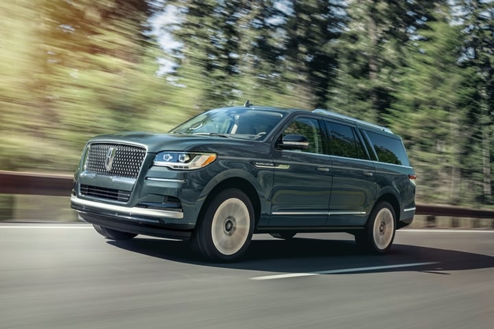 A 2023 Lincoln® Navigator SUV in Ocean Drive Blue is being driven up an incline surrounded by greenery