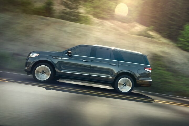 A profile of the 2023 Lincoln Navigator ® SUV in Ocean Drive Blue is being driven up an incline surrounded by greenery