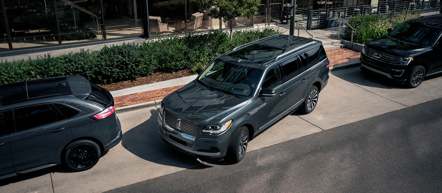 A 2023 Lincoln Navigator® SUV is being parallel parked between two cars on a downtown road outside a luxury hotel