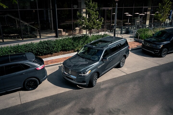 A 2023 Lincoln® Navigator SUV is being parked on the side of a downtown street in between two other vehicles
