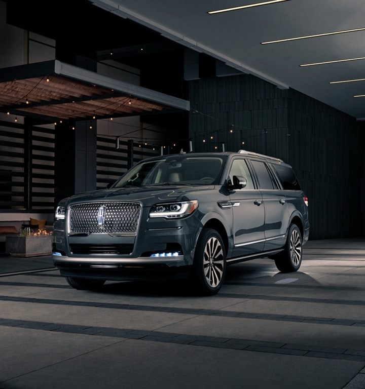 A man and woman in formal wear are approaching a 2023 Lincoln Navigator® SUV at night as it lights with the Lincoln Embrace
