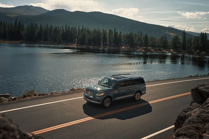 A 2023 Lincoln Navigator SUV is being driven along a lake in the mountains