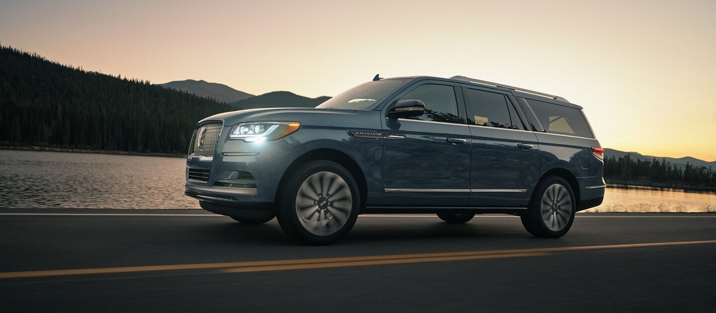 A 2023 Lincoln Navigator® SUV is being driven in the mountains while the setting sun washes over the reflective water