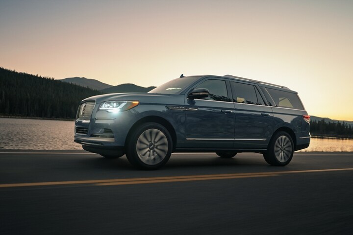 A 2023 Lincoln Navigator SUV is being driven in the mountains at sunset as light bounces off the calm waters