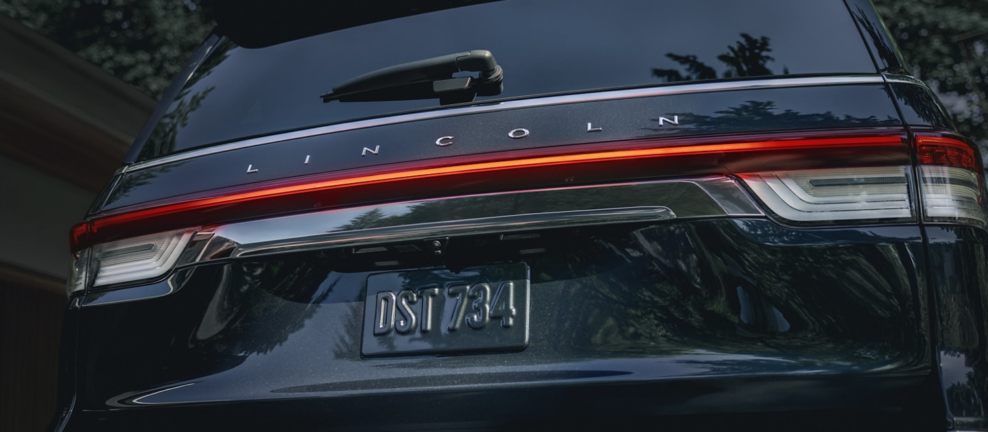 The rear LED taillamps of a 2024 Lincoln Navigator Reserve SUV illuminate with a red glow at night