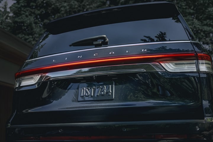 The rear LED taillamps of a 2024 Lincoln Reserve SUV illuminate with a red glow at night