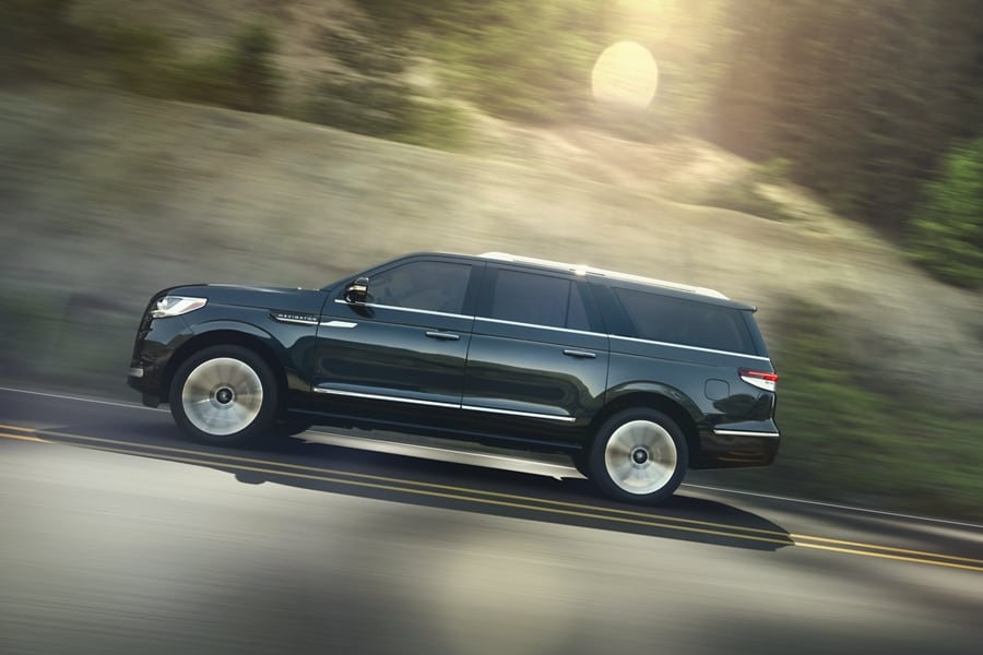 A 2024 Lincoln Navigator SUV in Flight Blue being driven up an incline surrounded by greenery